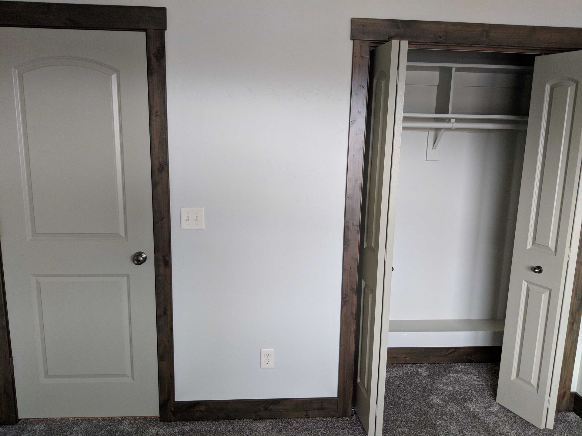 A wall featuring a standard room door on the left and an open closet with a shelf on the right, both with dark wood trim.