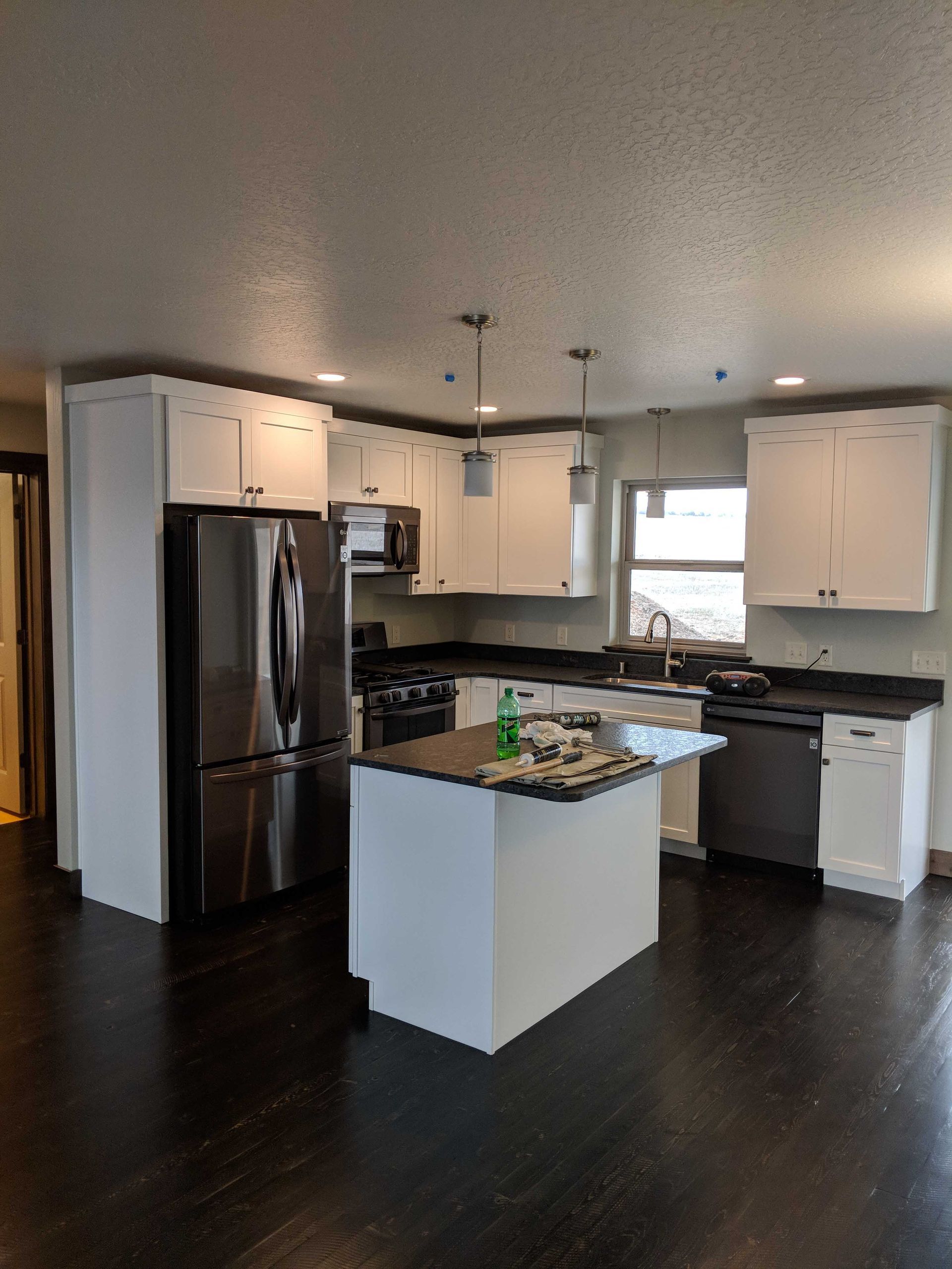 Modern kitchen with white cabinets, dark countertops, stainless steel appliances, a center island, and dark wood flooring.