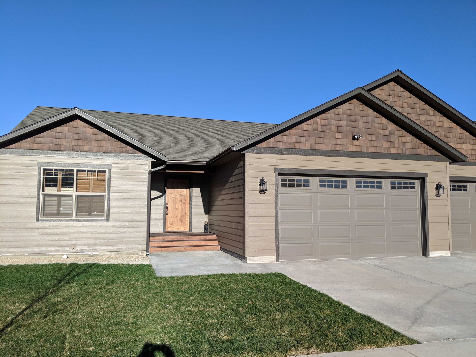 A modern single-story house with a tan horizontal-sided exterior, dark brown shake accents, and an attached two-car garage.