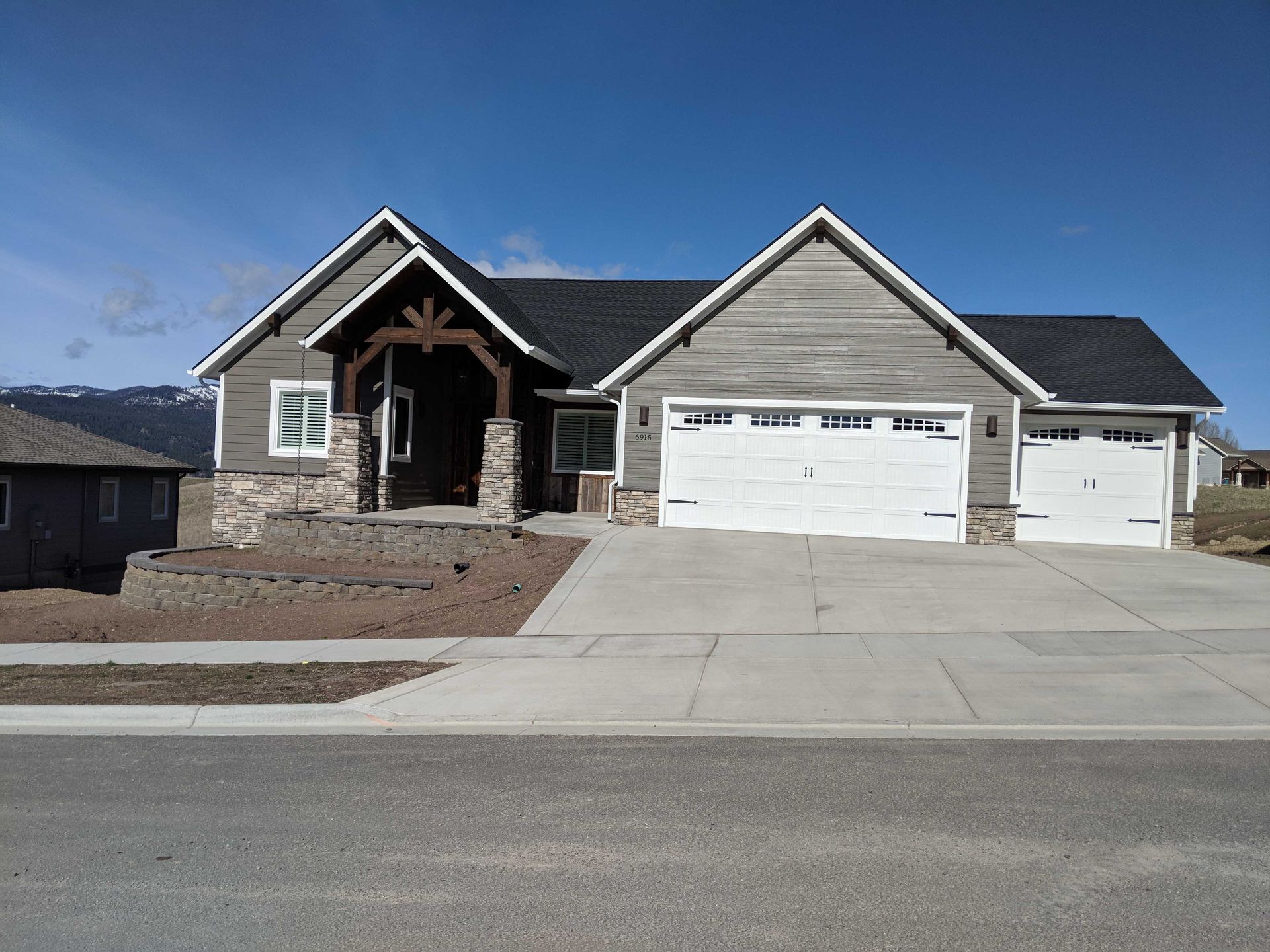 A one-story suburban house with gray horizontal siding, stone accents, a three-car garage, and a peaked entryway.