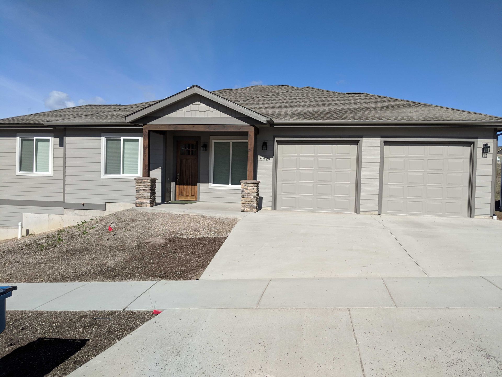 A single-story grey house with a two-car garage, brown wooden front door, stone accents, and a concrete driveway.