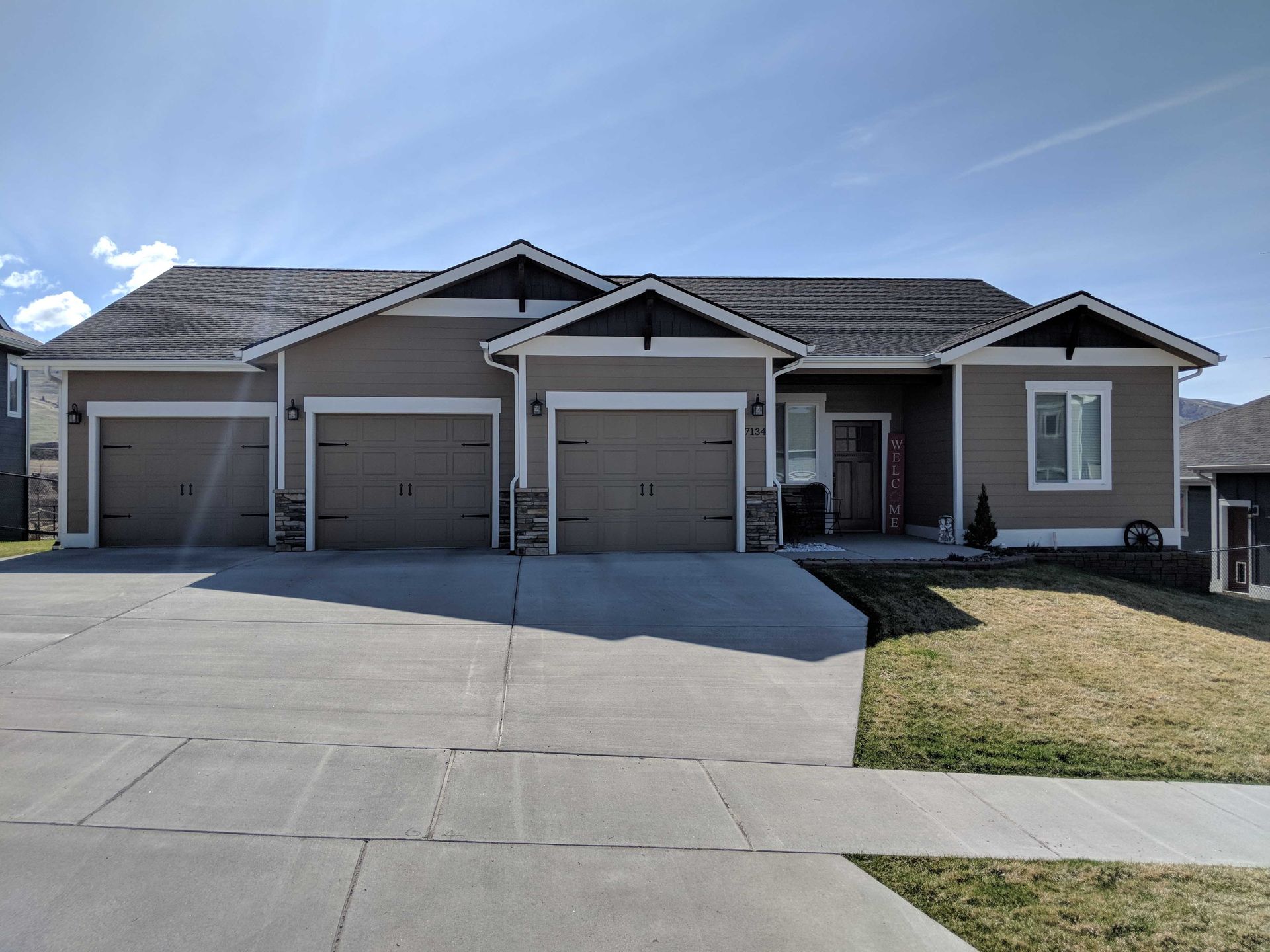 A tan, single-story house with a three-car garage and dark brown trim under a clear blue sky.