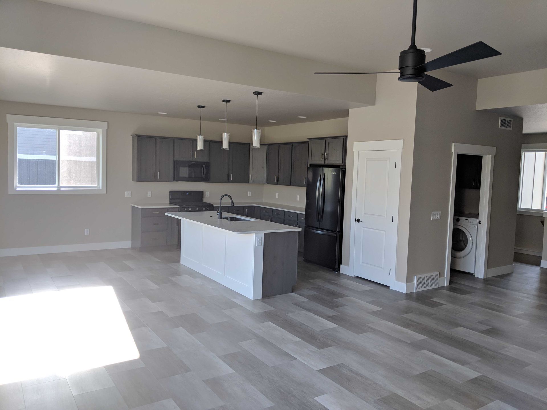 A modern, open-concept kitchen featuring a white island, gray cabinets, stainless steel appliances, and wood-look flooring.