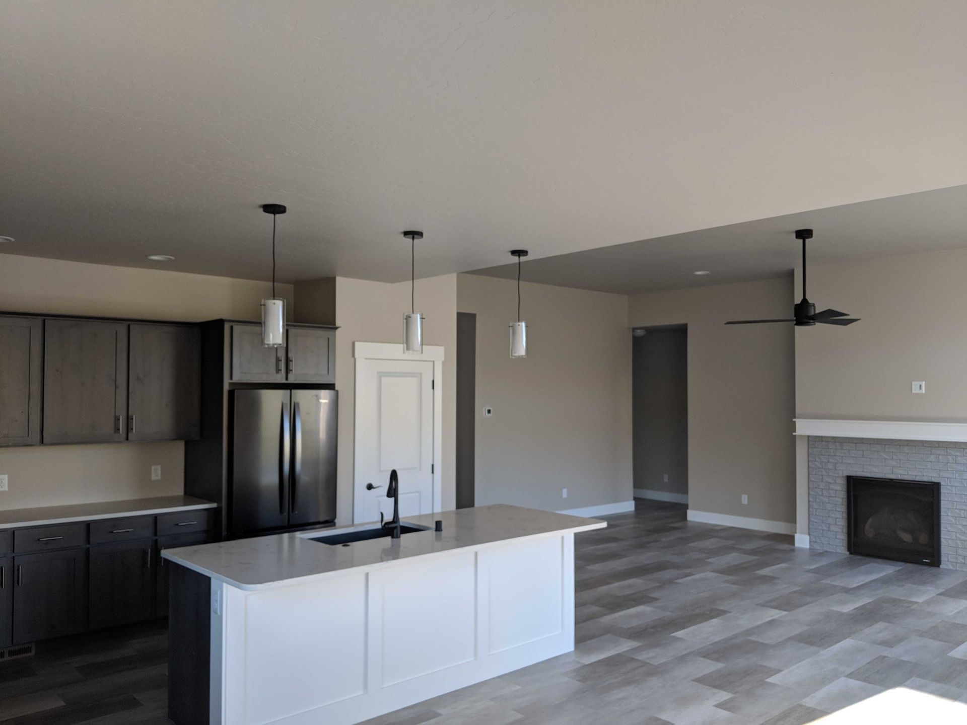 Modern kitchen with dark cabinets, a white island, stainless steel refrigerator, and living area with a fireplace.