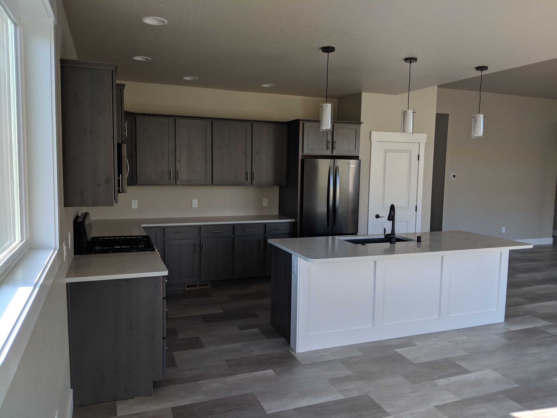 Modern kitchen with dark grey cabinets, a white island, stainless steel appliances, and wood-look flooring.