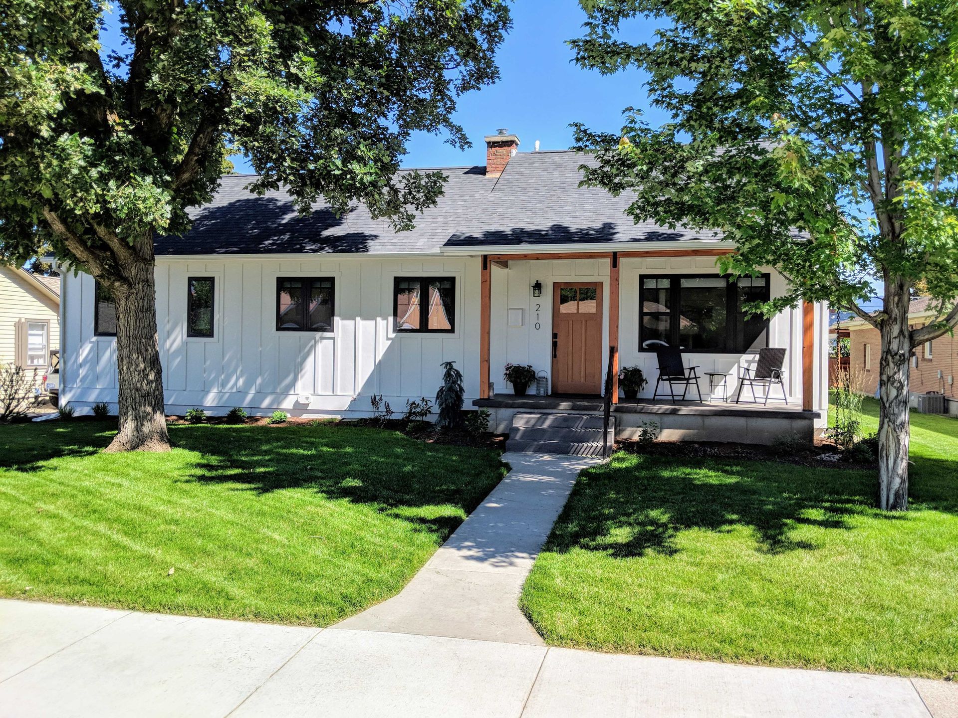 A white cottage-style house with dark-framed windows, a wood front door, and a covered porch, set behind a green lawn.