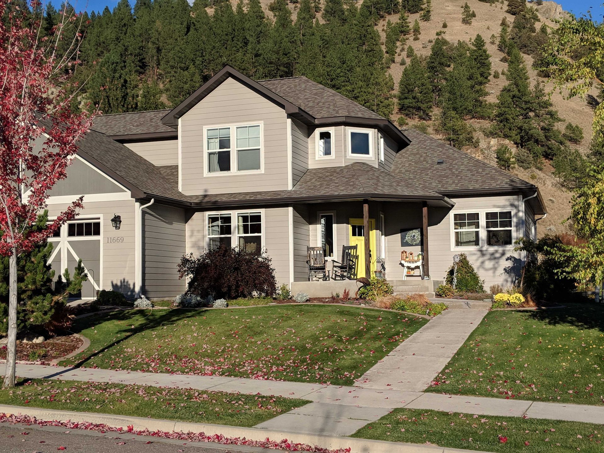 A beige two-story suburban house with a yellow front door and an attached garage, set against a tree-covered hillside.