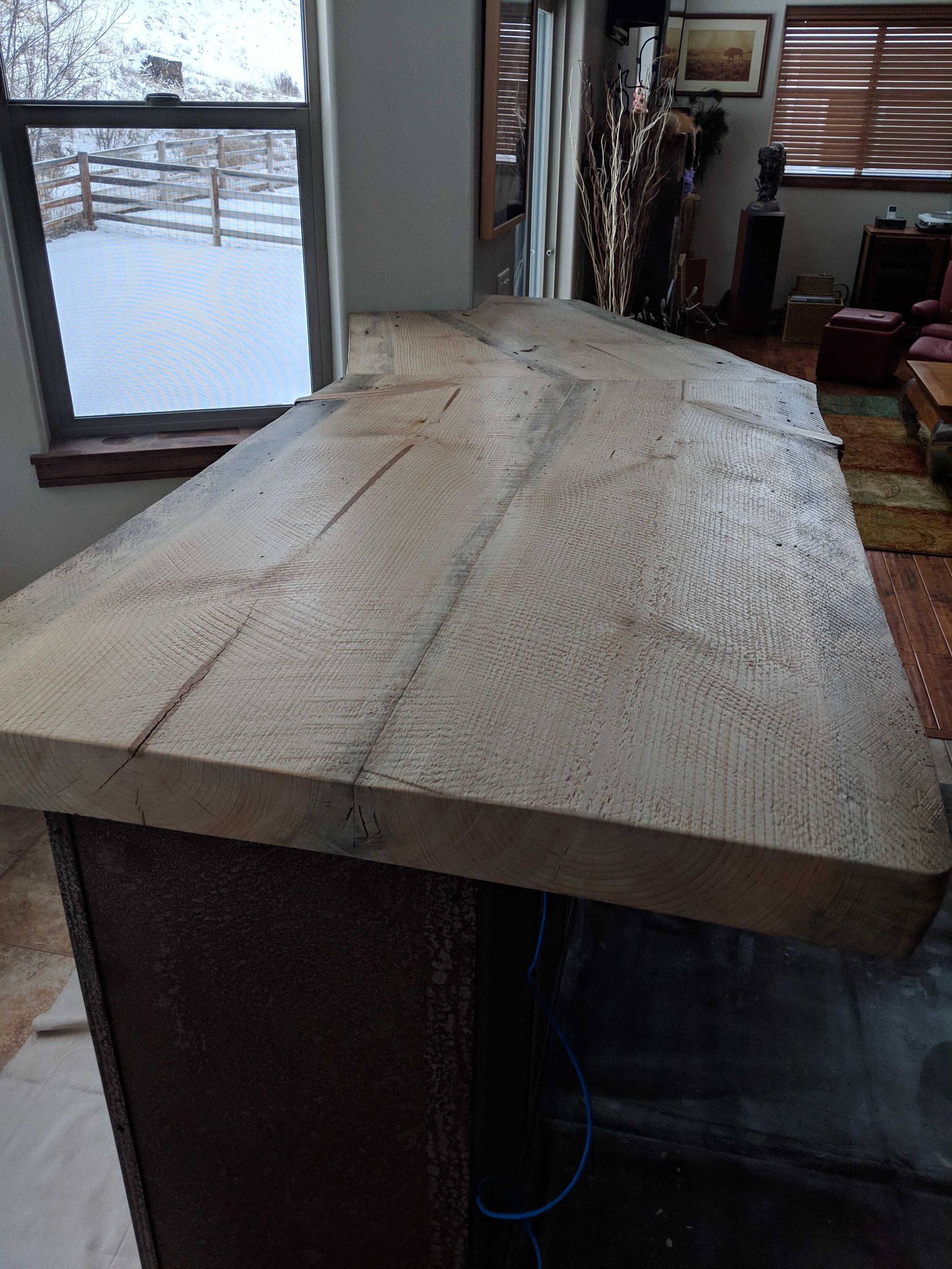 A wide wooden countertop with a natural live edge, installed over dark cabinetry in a room with a view of snowy outdoors.