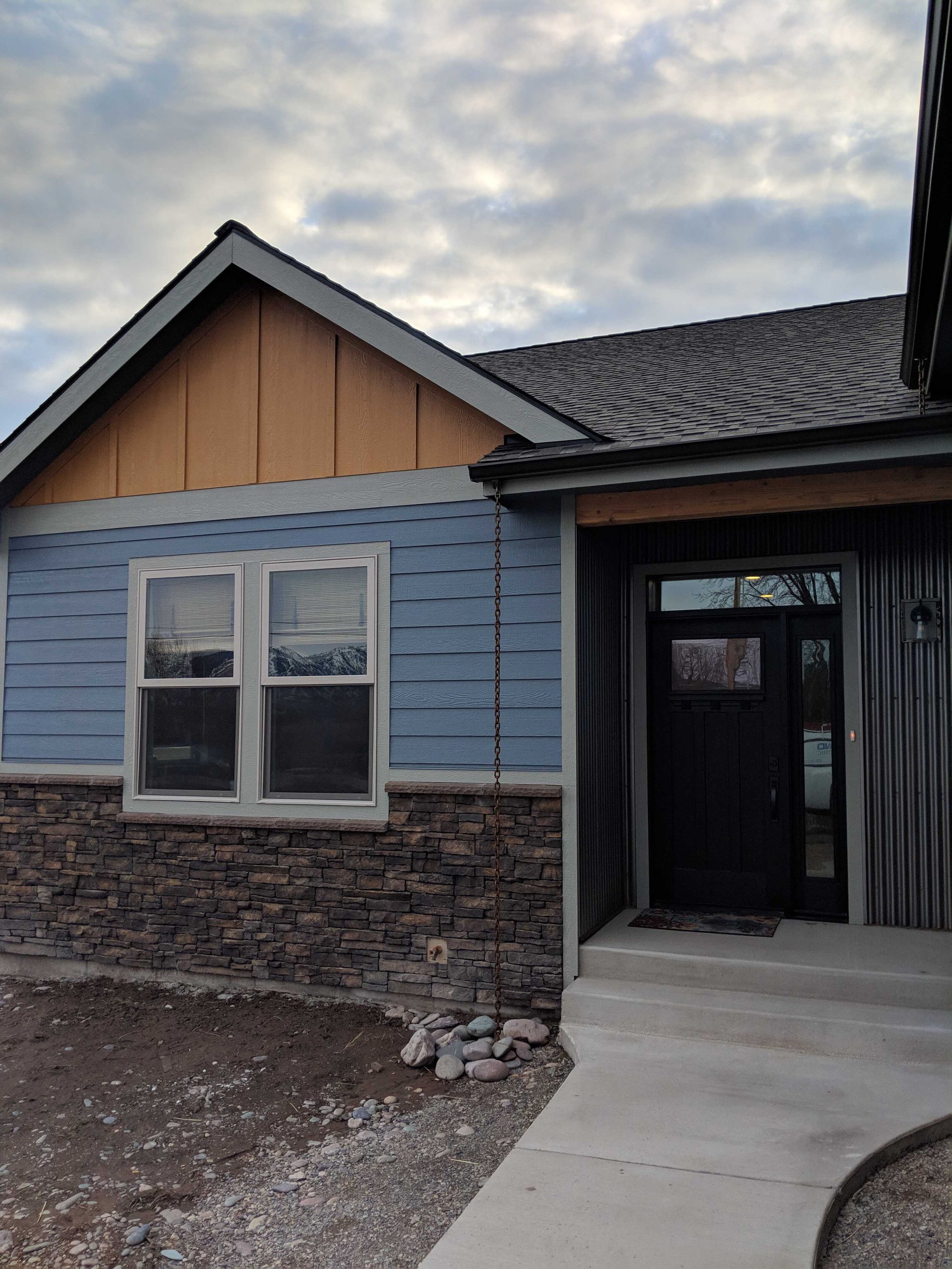 A single-story home exterior with a blue horizontal-siding wall, stone base, orange gable, and a black front door.