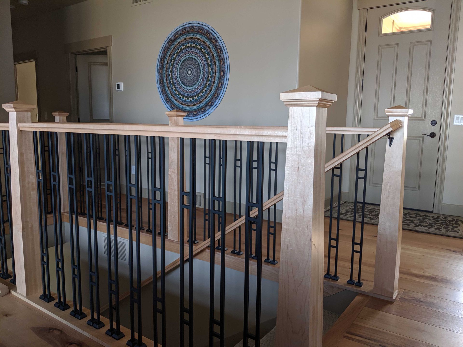 A staircase landing with a light wood railing and black metal balusters, featuring a circular blue wall art piece nearby.