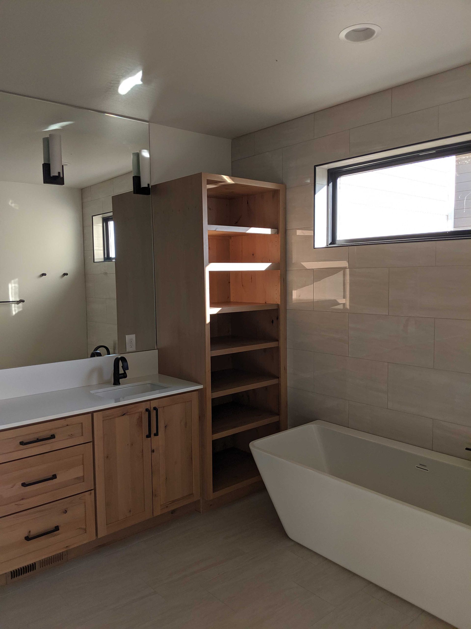Modern bathroom with wood vanity, open shelving, a large mirror, and a freestanding white bathtub.
