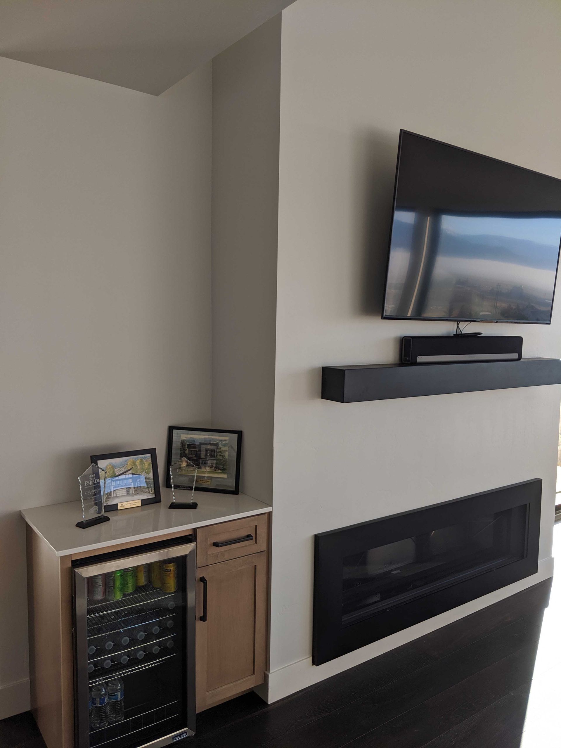 A modern living room with a wall-mounted TV above a fireplace, beside a small cabinet featuring a built-in beverage fridge.