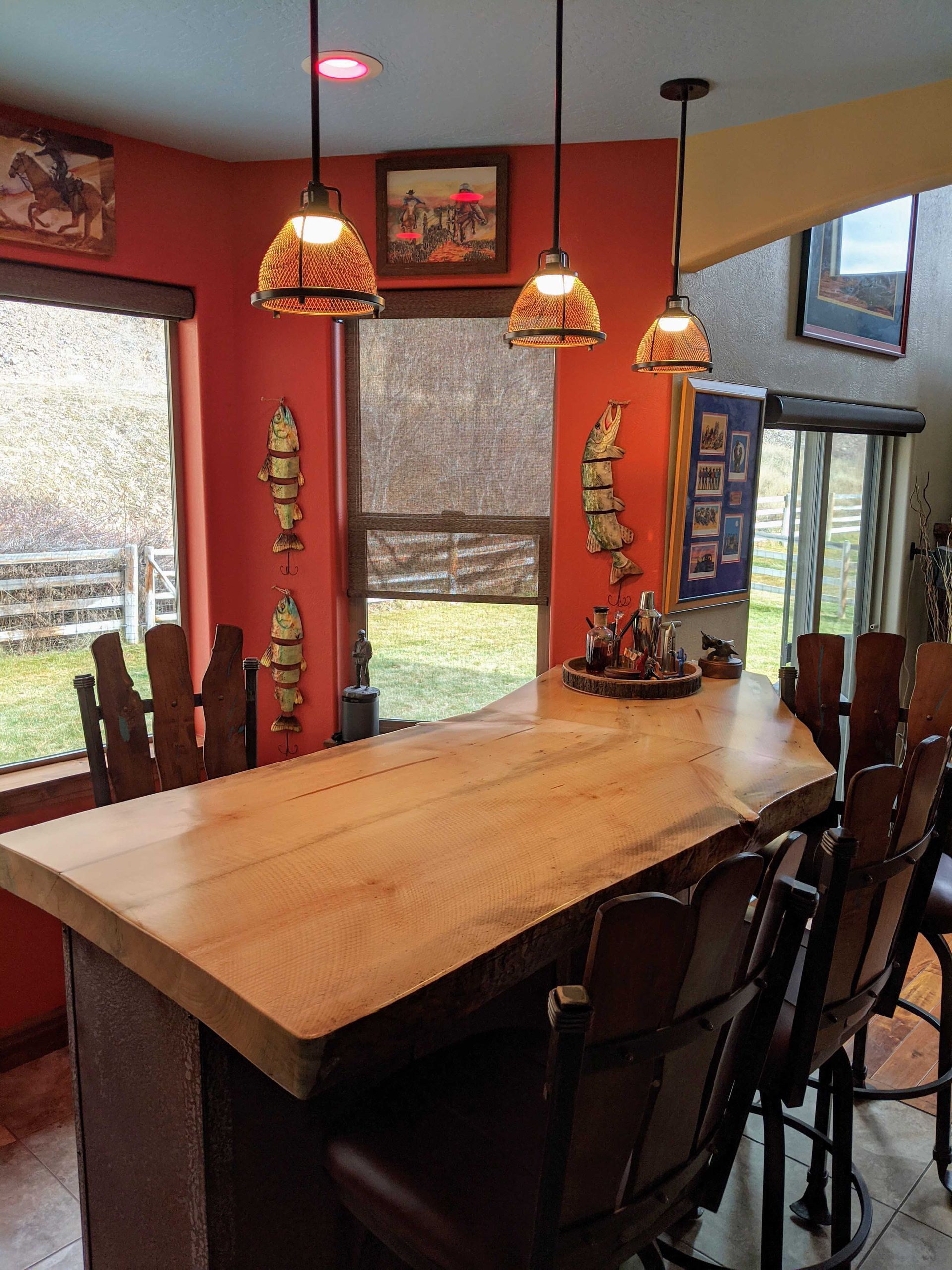A wooden live-edge bar with bar stools in a room with orange walls, three pendant lights, and western-themed decor.