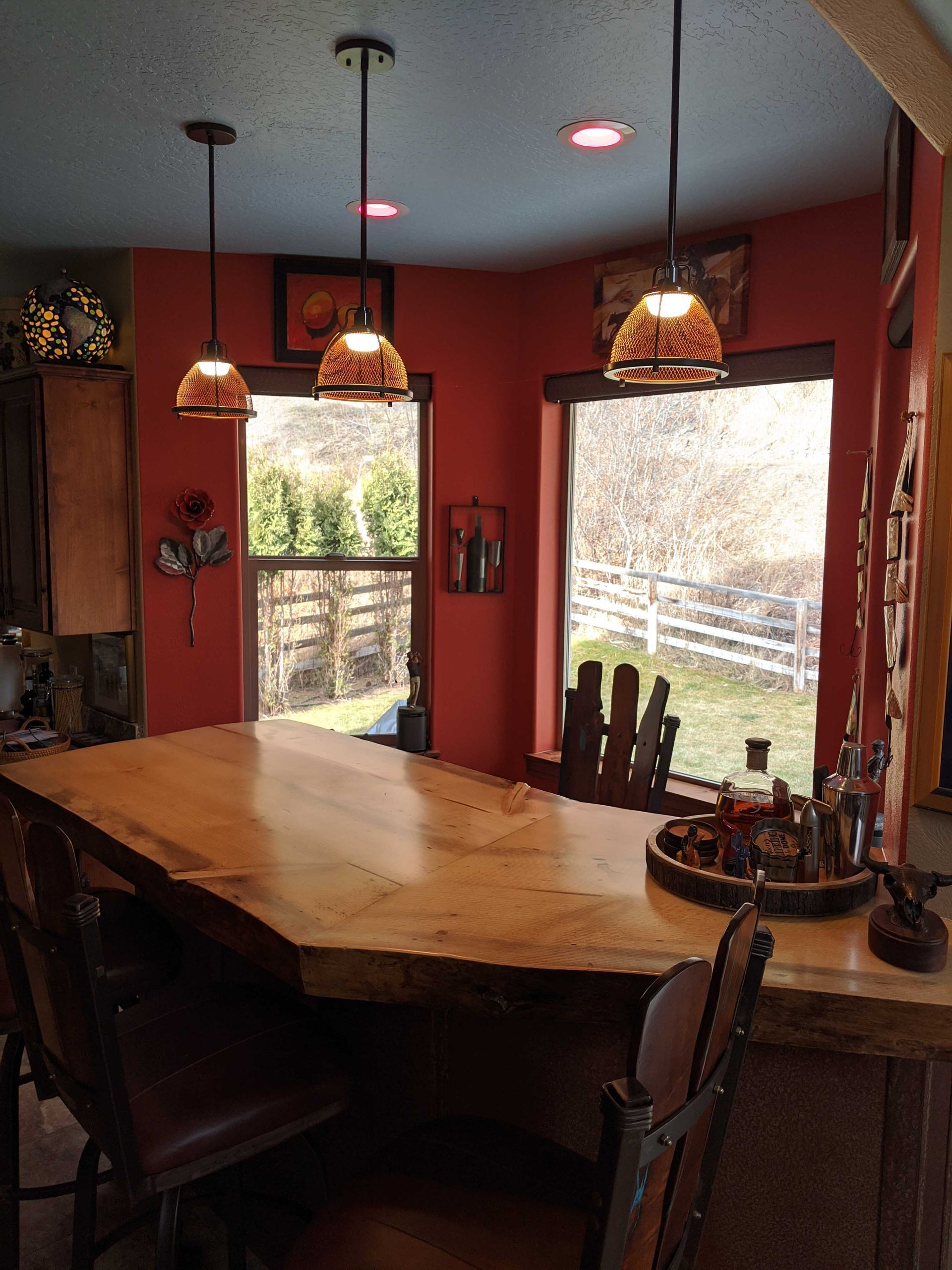 A rustic kitchen island with a live-edge wooden countertop under three pendant lights, set against a terracotta-red wall.