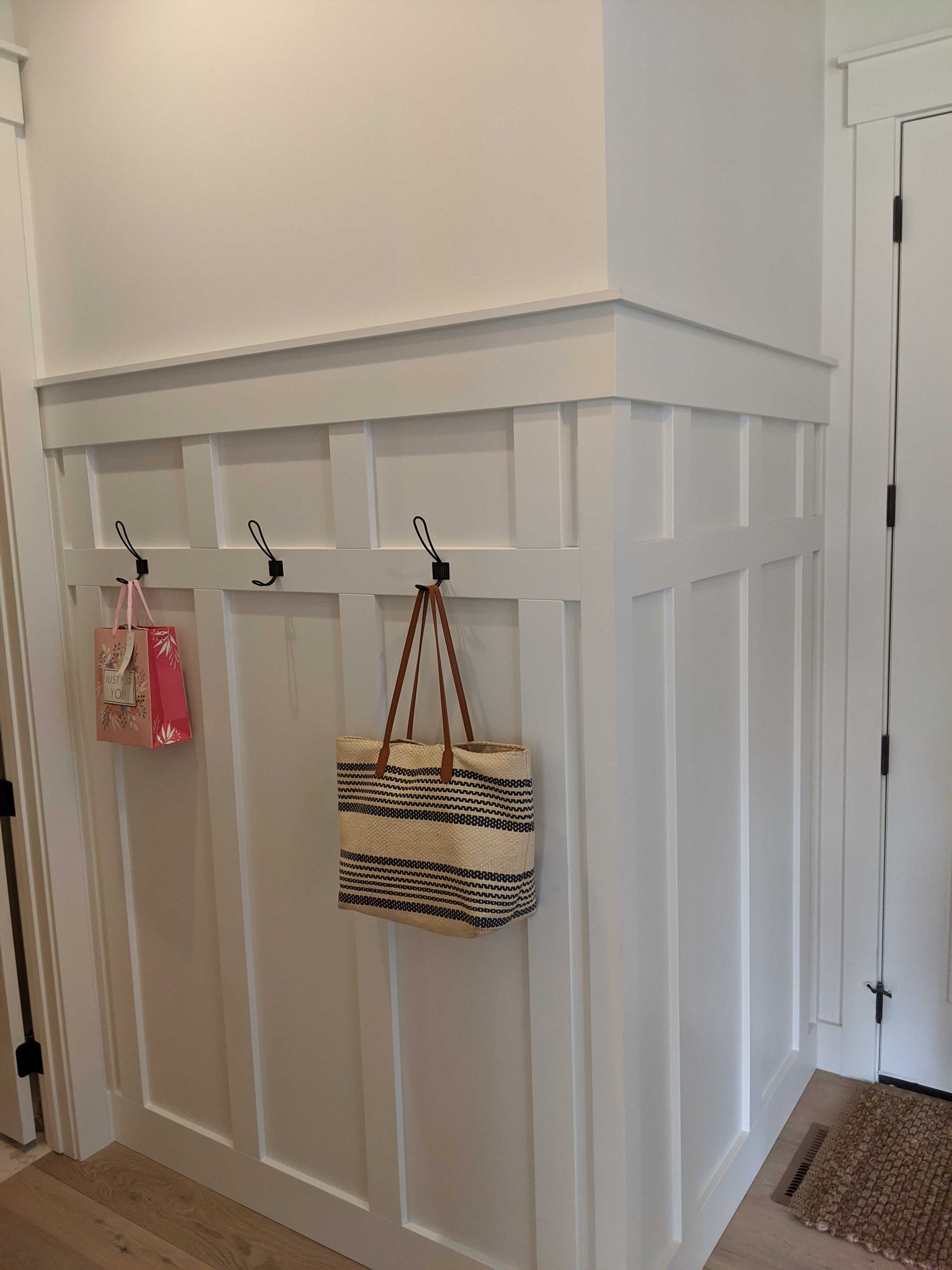 White wainscoting wall paneling with hooks holding two handbags in a residential entryway.