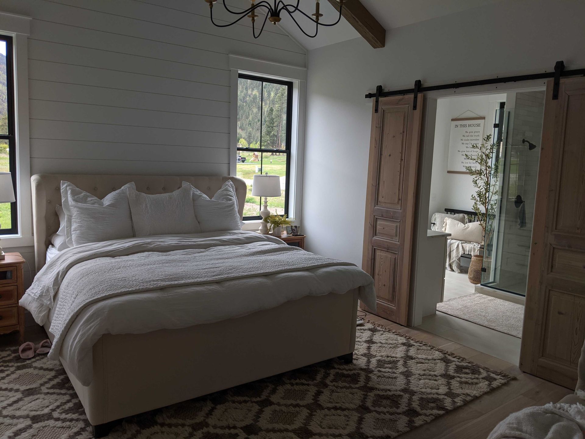 A modern bedroom with a tufted bed, white bedding, horizontal wall planks, and wooden sliding barn doors to a bathroom.