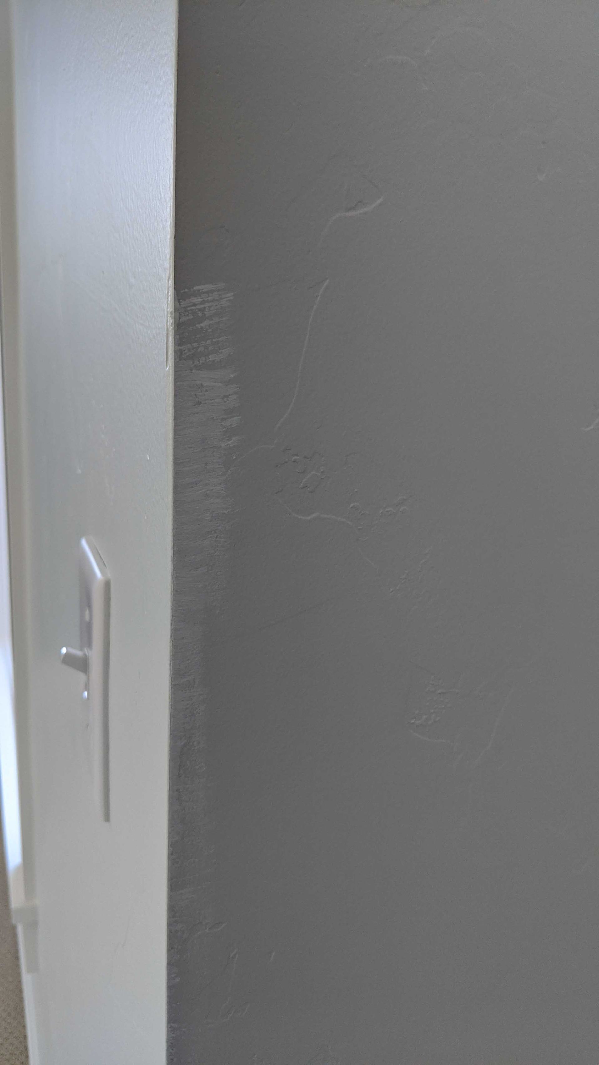 A light switch on a corner wall with a visible scuff mark and wear along the vertical edge.