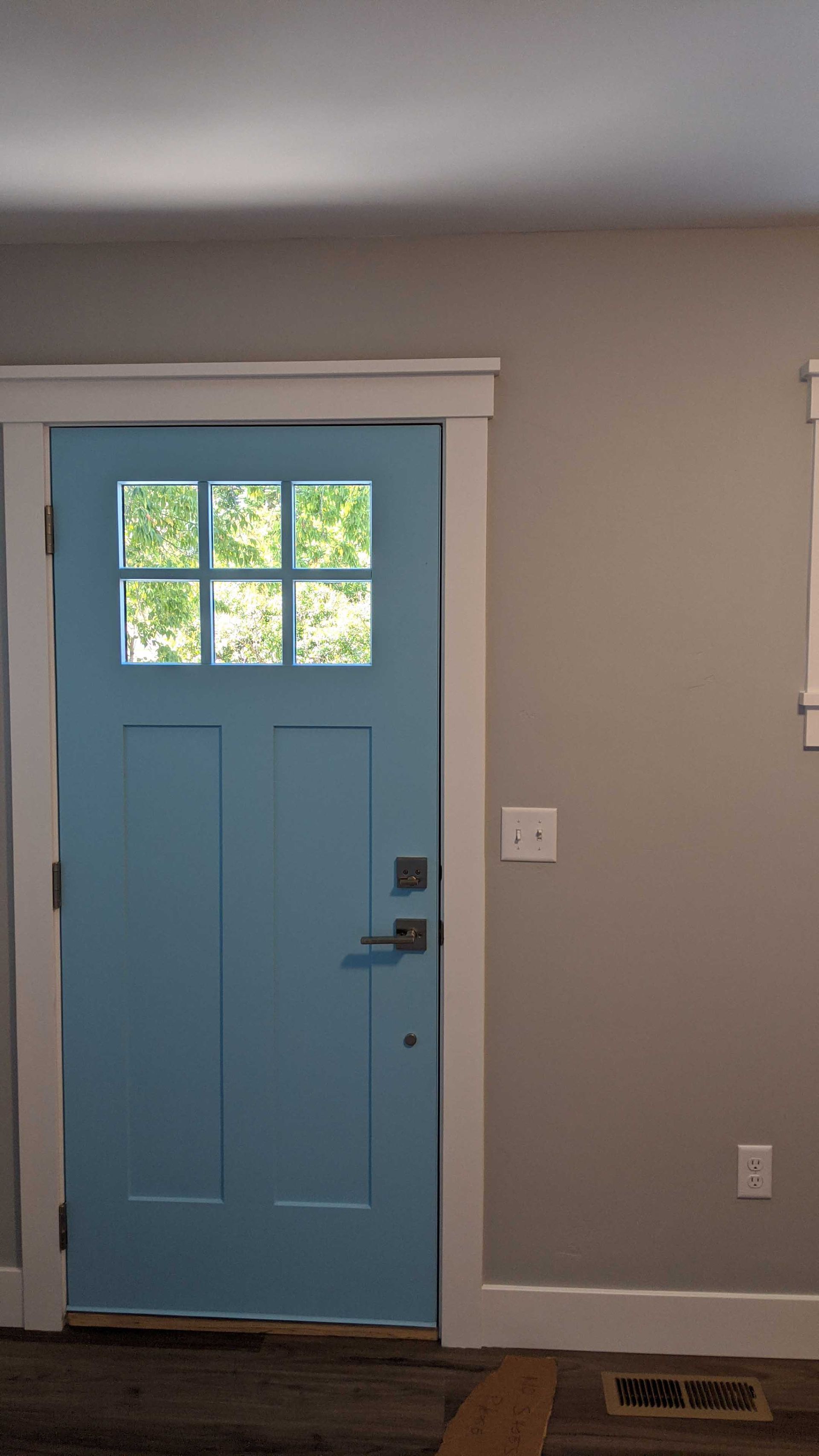 A bright blue door with a six-pane window set in a white frame against a gray wall.