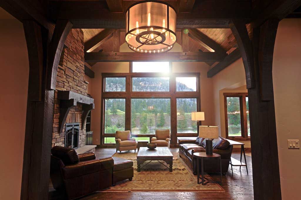 A living room with a stone fireplace, exposed wood beams, and a large window view, framed by dark wooden archways.