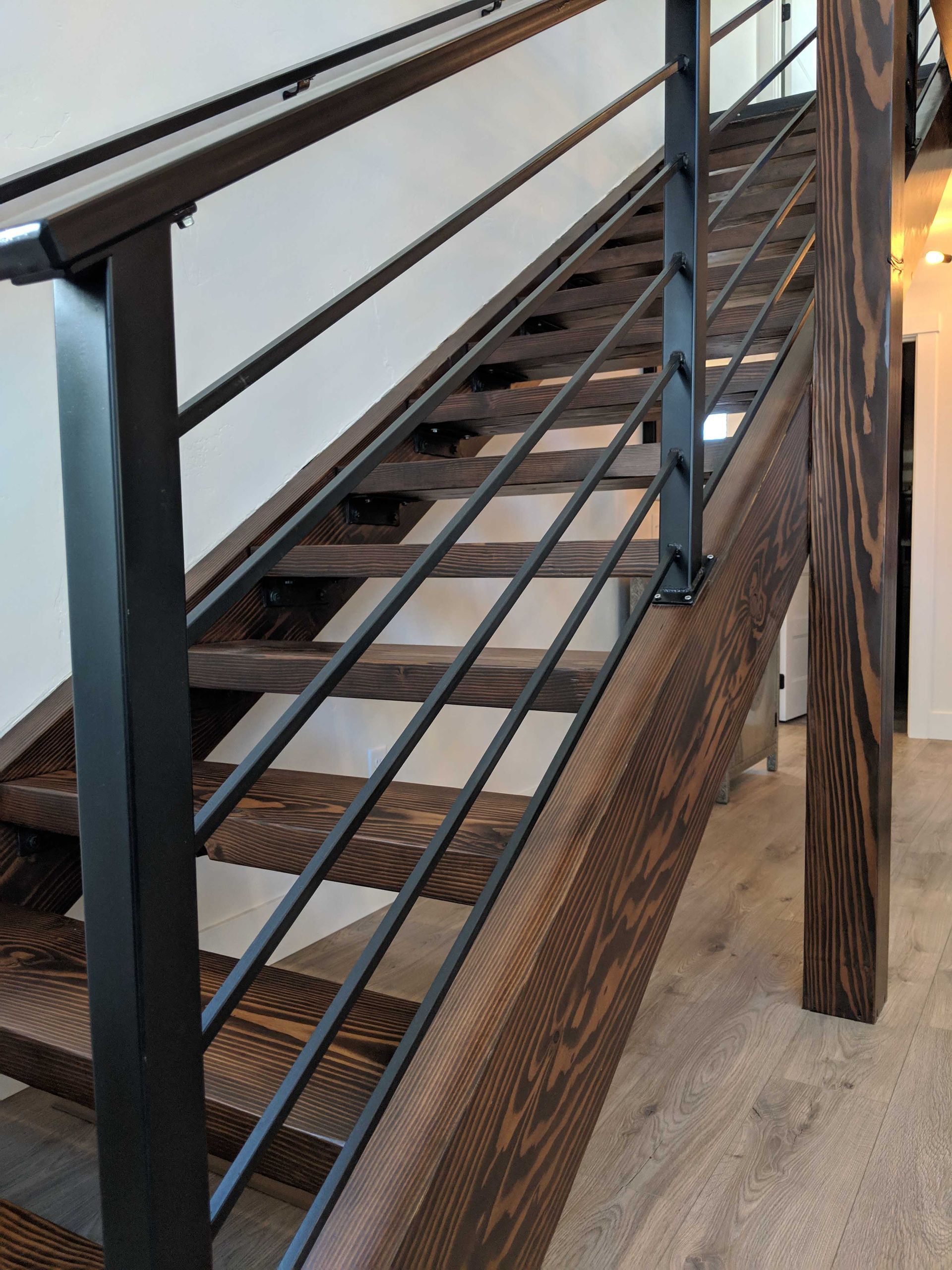 Staircase with dark-stained wooden steps, a matching wooden post, and a sleek black metal railing with horizontal bars.