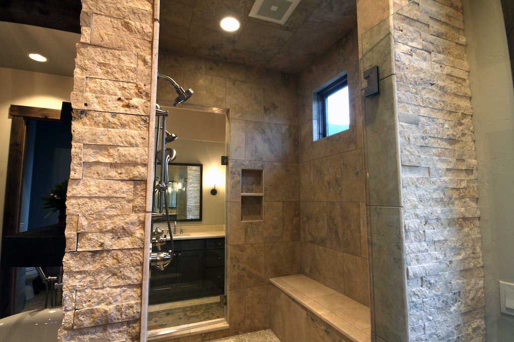 A walk-in shower with textured stone walls, a bench, a built-in shelf, and a shower head.