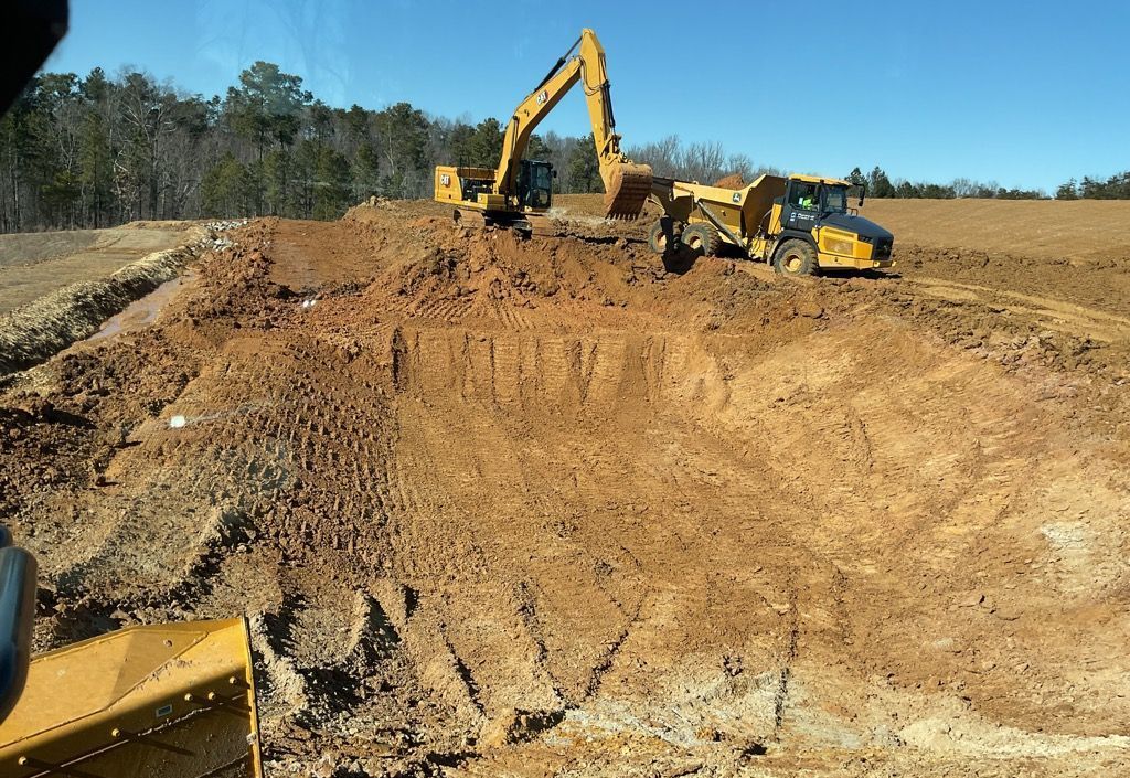 A yellow excavator loads dirt into a yellow articulated dump truck at a sunny, open-pit construction site.