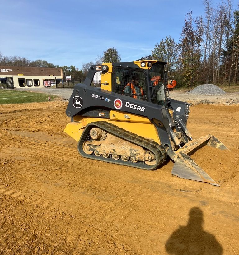 A yellow and black John Deere compact track loader pushes dirt at a construction site on a sunny day.