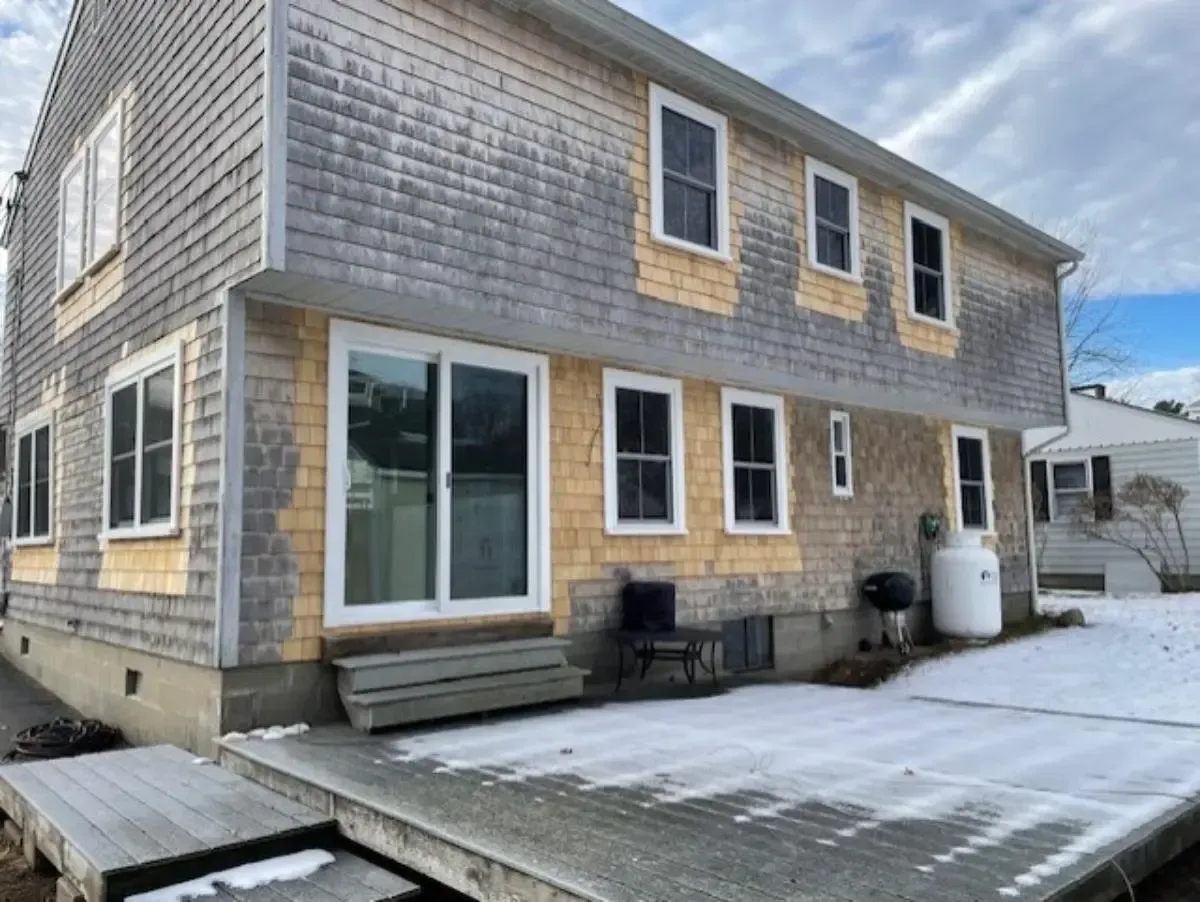 Two-story house with weathered cedar shingle siding and a snow-covered deck.