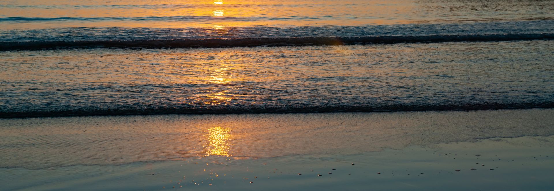 The sun is reflected in the water on the beach at sunset.