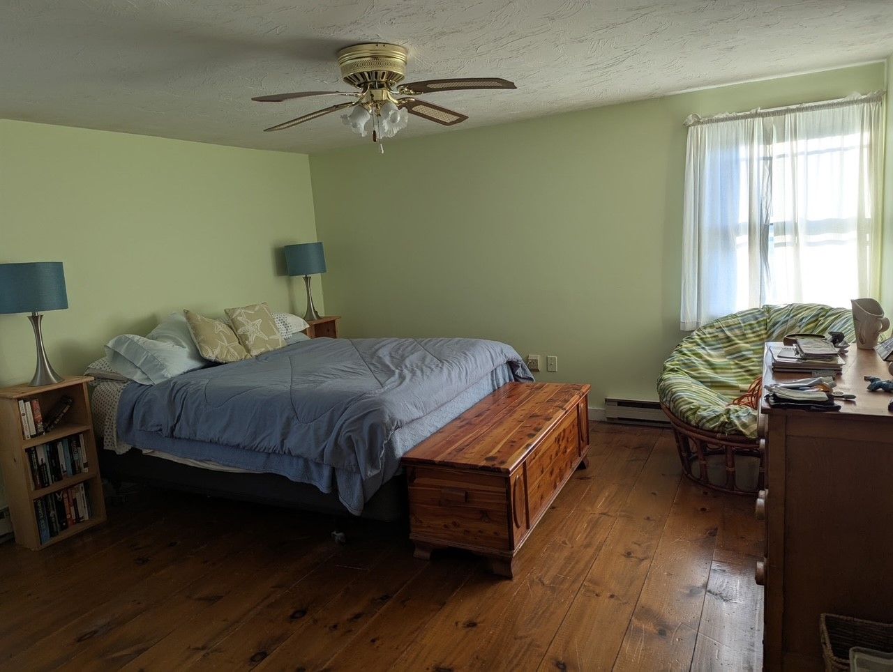 A bedroom with a bed , dresser , chair and ceiling fan.