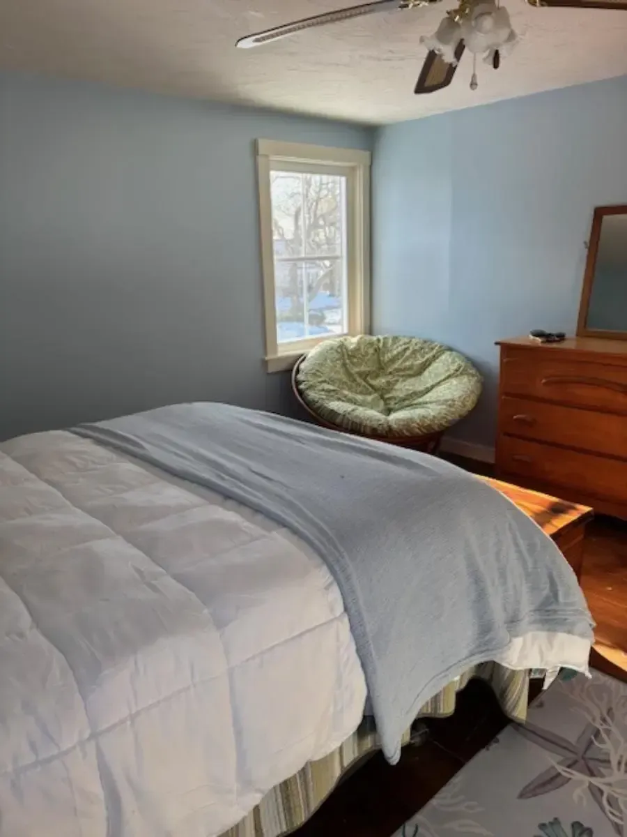 Bedroom with blue walls, a bed with a light blue blanket, and a green papasan chair near a window.