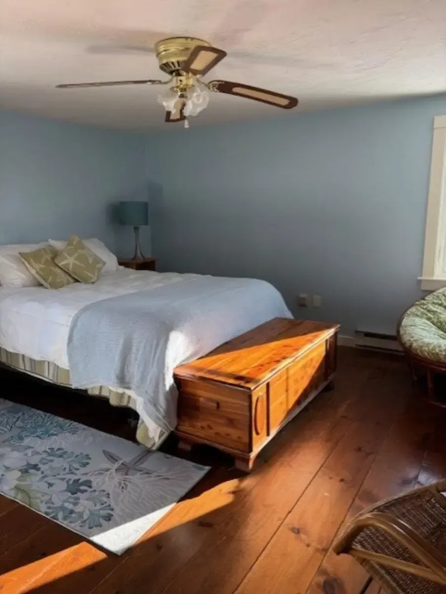 Bedroom with blue walls, hardwood floor, bed with white bedding, and a wooden chest.