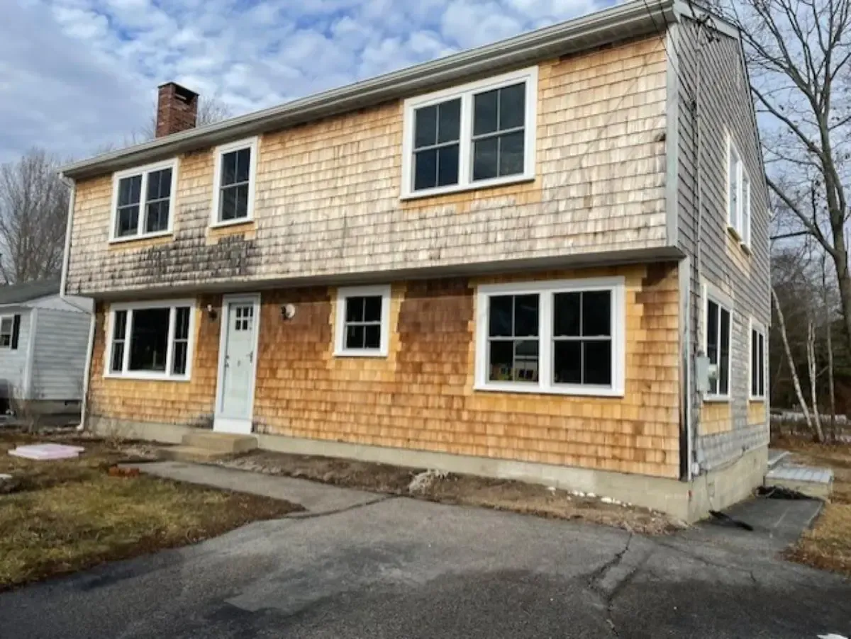 Two-story house with weathered cedar shake siding. New white windows and front door. Gray concrete foundation.