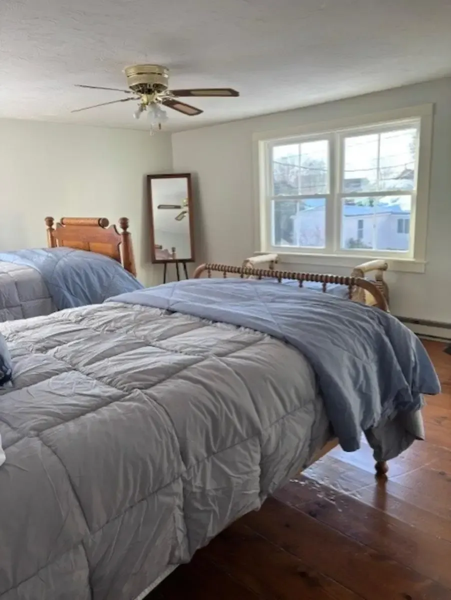 Two beds with blue and gray bedding in a room with a mirror and window.