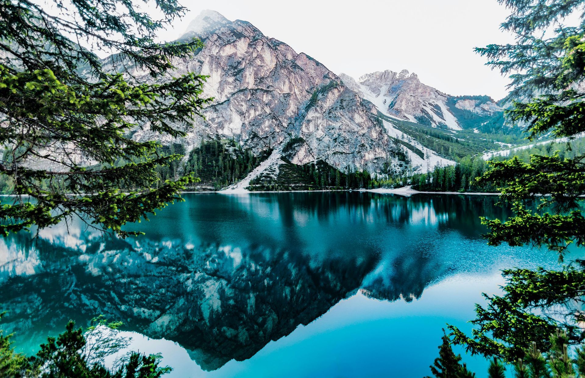 Mountain range reflected in a turquoise lake framed by evergreen trees.