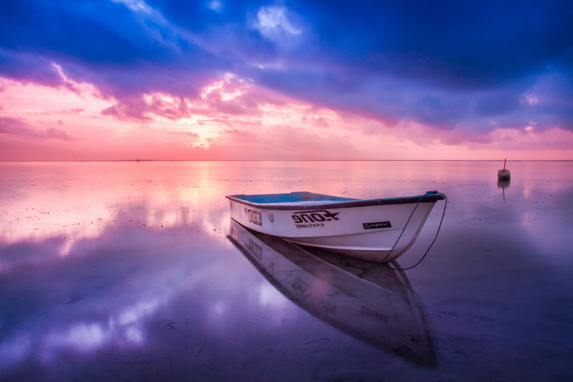 Boat floats on still water, reflecting the purple and pink sunset sky.