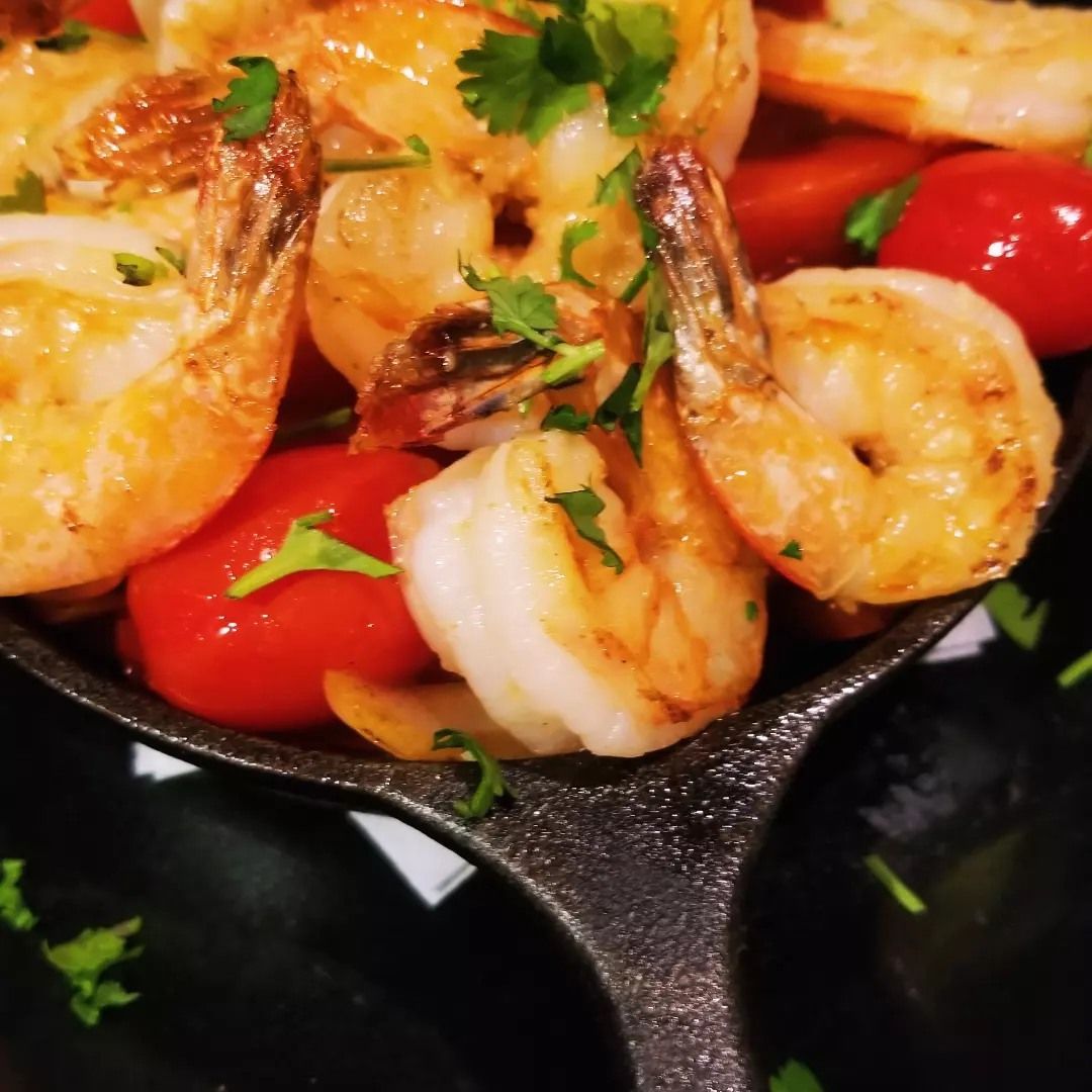 A skillet filled with shrimp and tomatoes on a table.