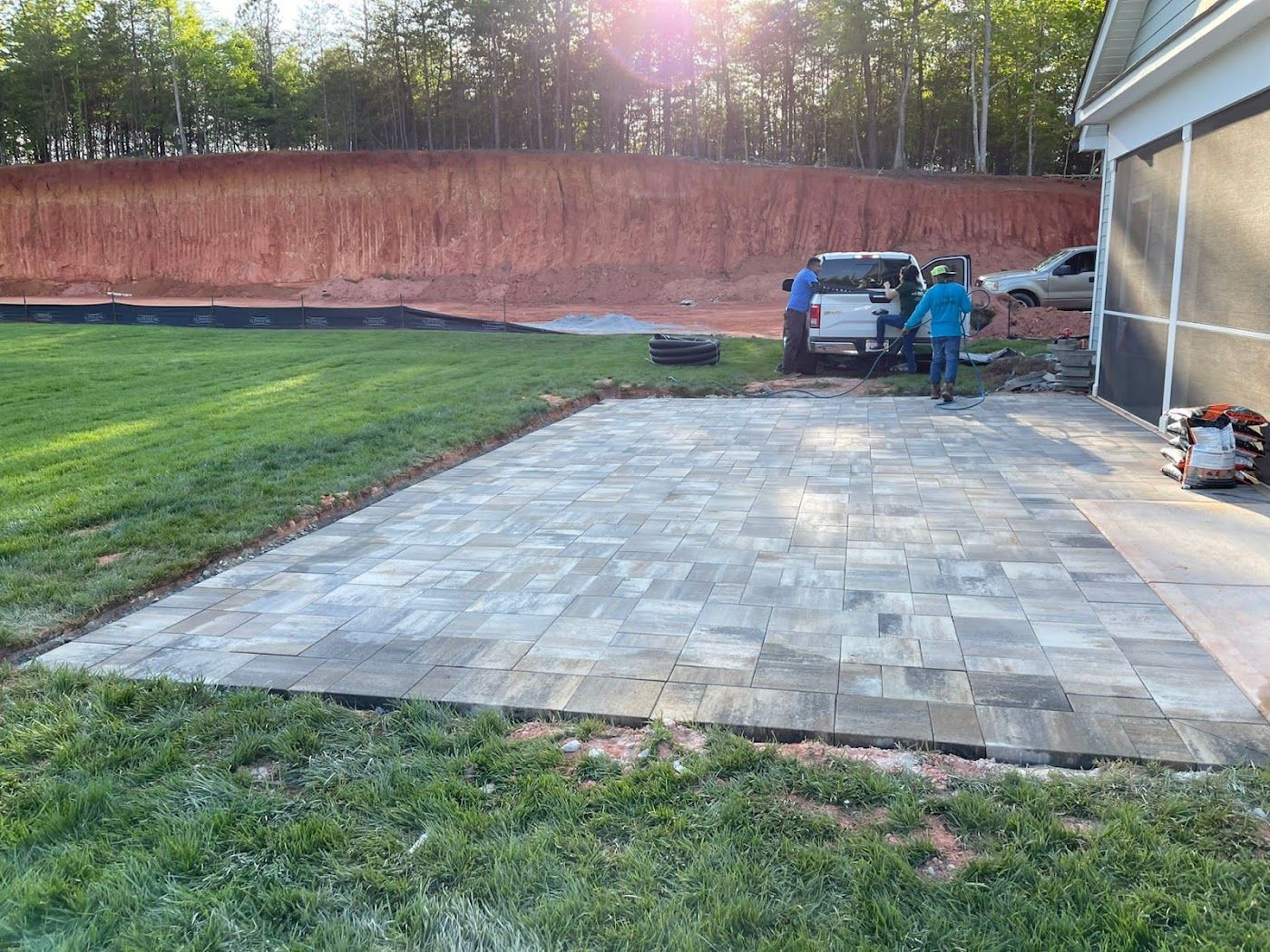 Completed paver patio next to a house with people and a vehicle on a construction site.