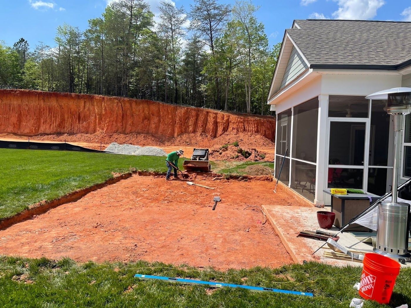 Construction site: Excavator leveling ground for patio next to a house with a screened porch. Orange soil.
