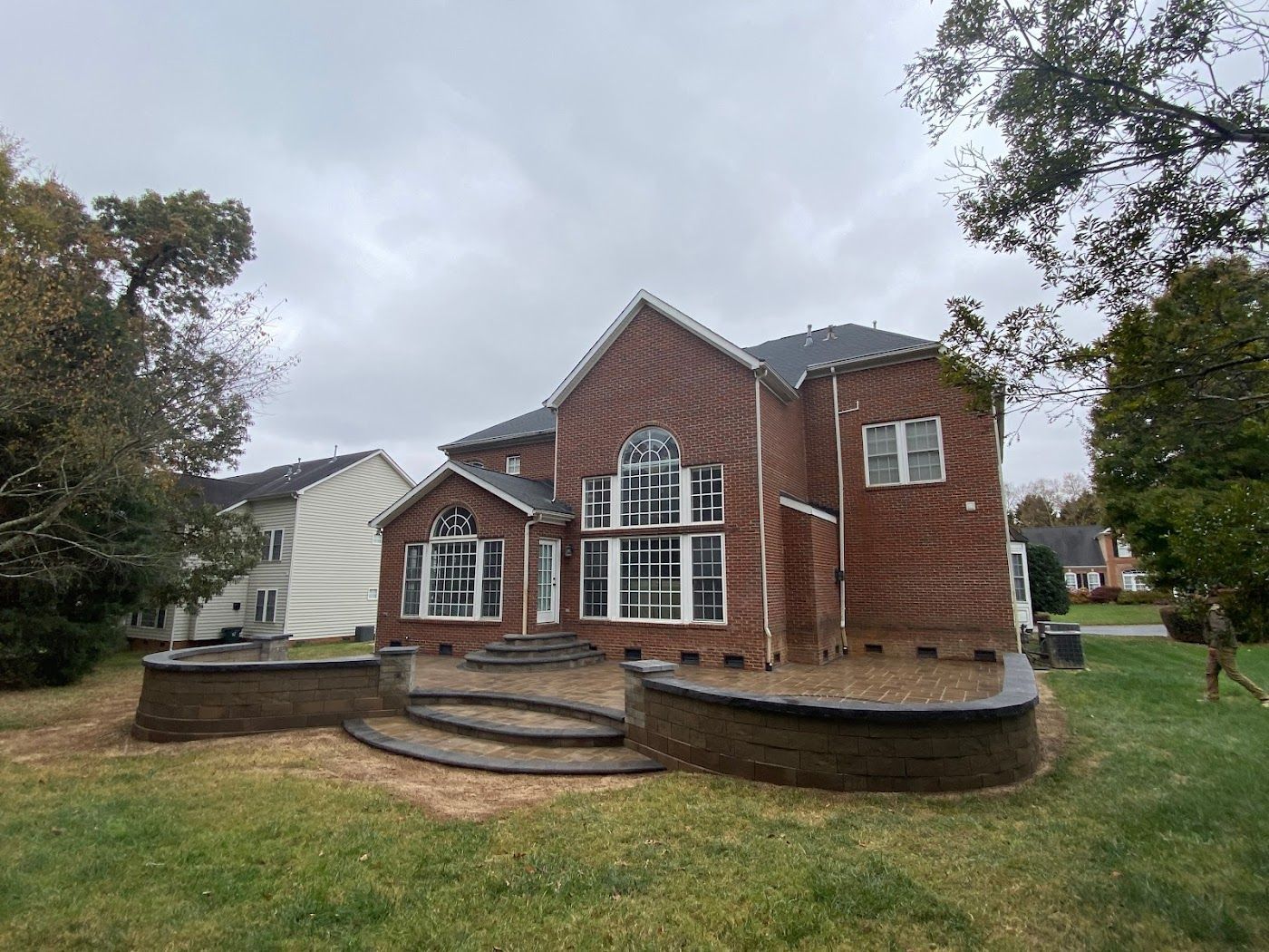 Red brick house with large windows, curved retaining wall, and green lawn under a cloudy sky.