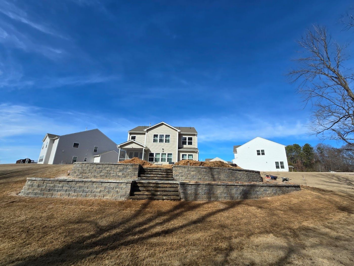 A house on a hillside with stone retaining walls and stairs, under a bright blue sky.
