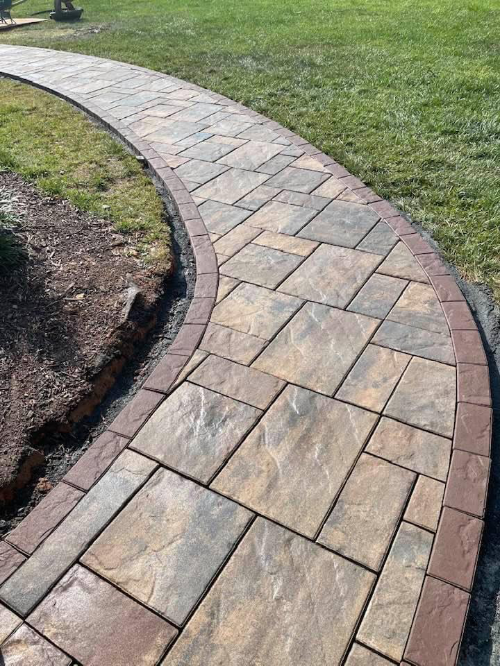 Curved stone walkway with brown border, through green grass.