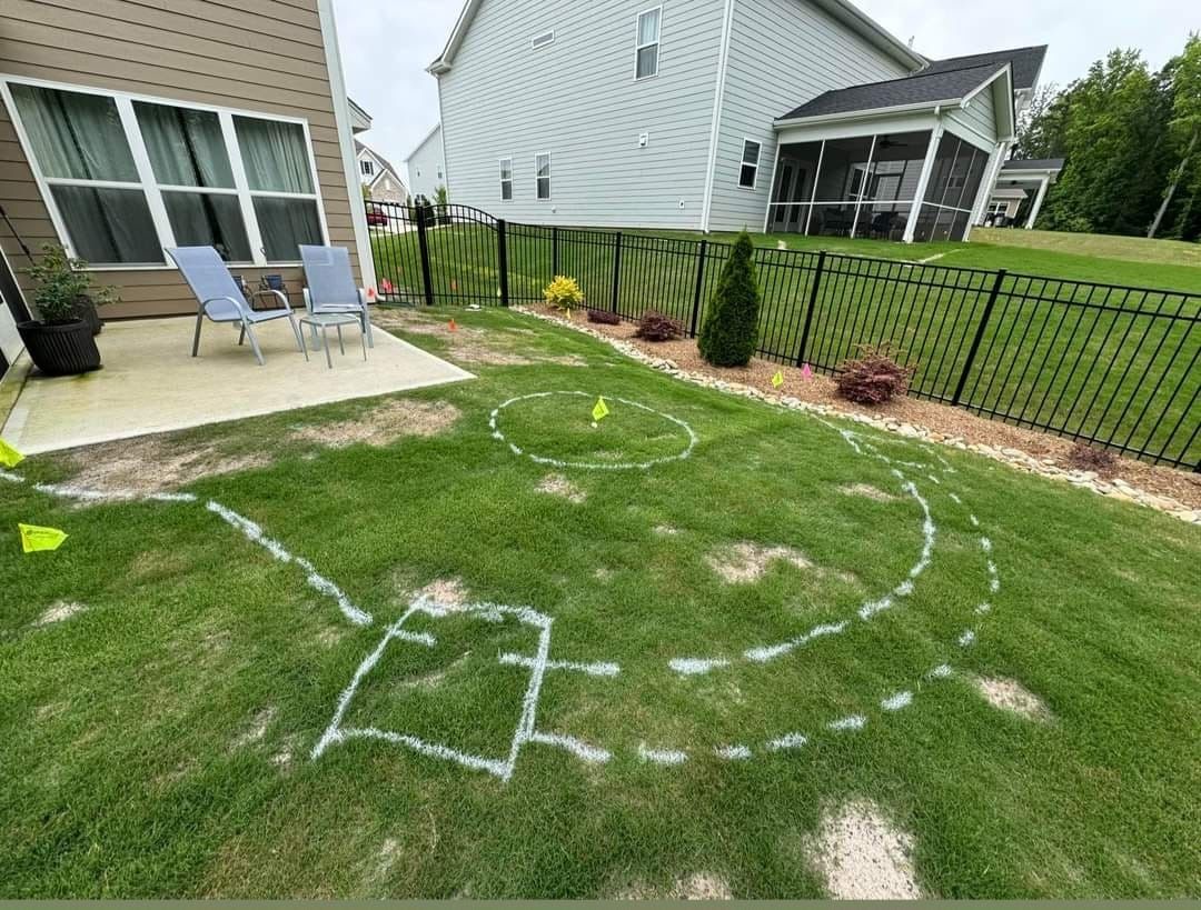 A backyard lawn marked with chalk lines, a patio, and a fence. The lines create shapes for a yard game.