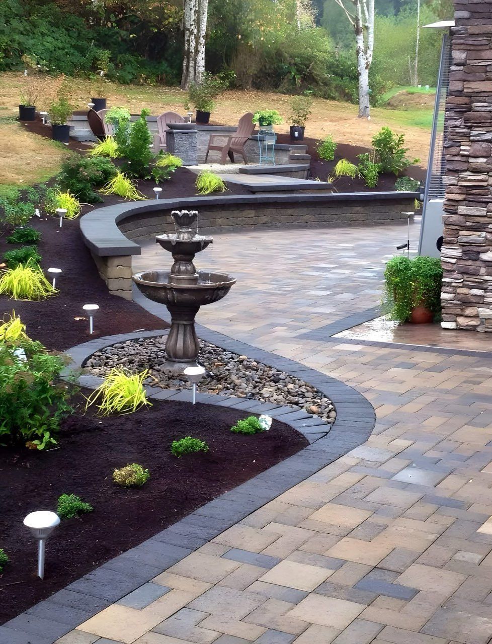 Stone patio with a tiered fountain, landscaping, and outdoor lighting.