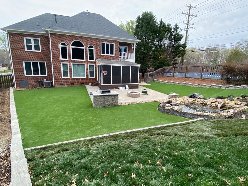 Backyard with a brick house, screened porch, artificial turf, stone patio with fire pit, and pond.