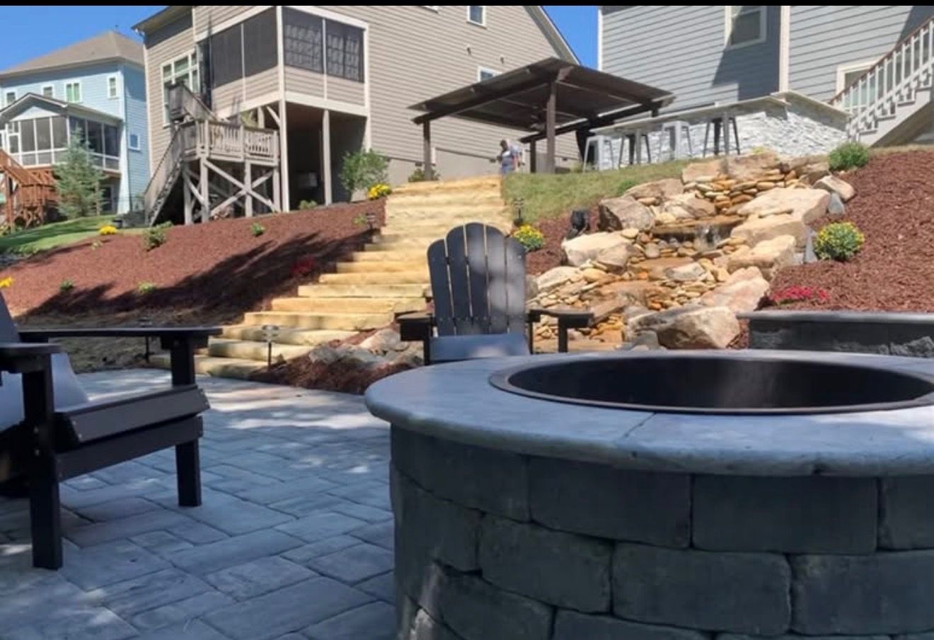 Backyard patio with fire pit, stone steps, waterfall feature, and Adirondack chairs.