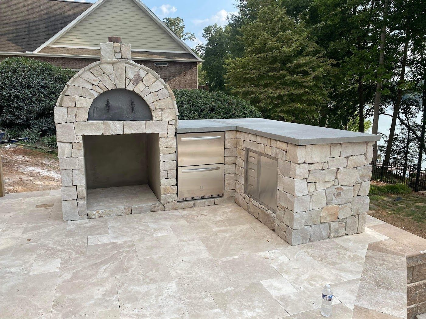 Outdoor stone pizza oven and grilling station on a patio. Includes a stainless steel door and countertop.