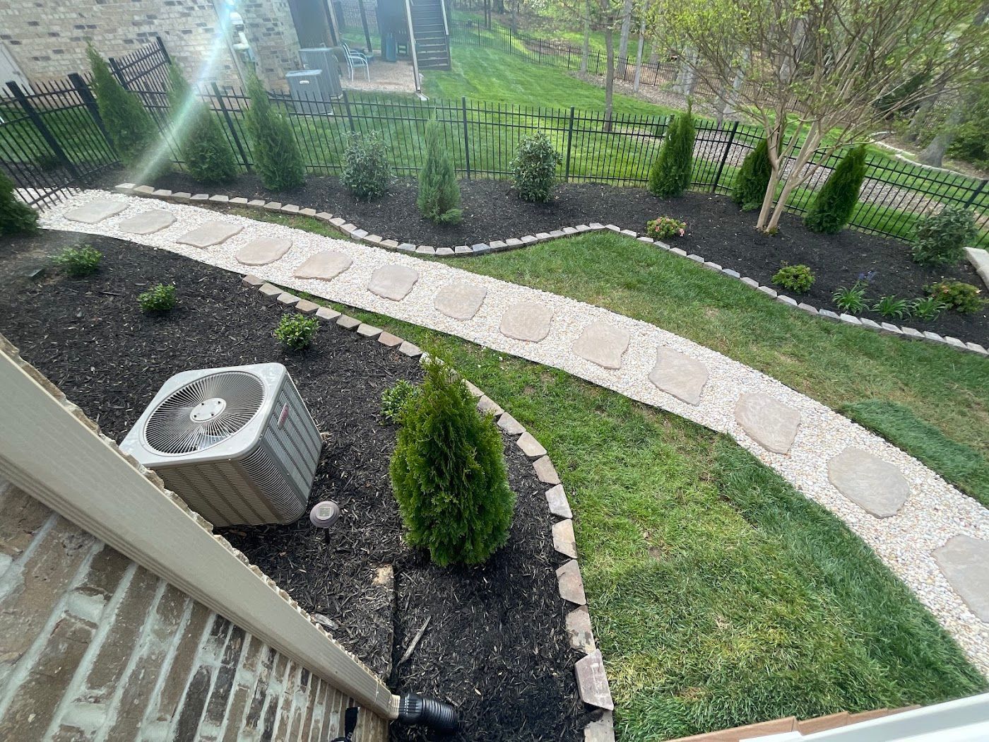 Stone pathway winds through landscaped yard with grass, bushes, and trees.