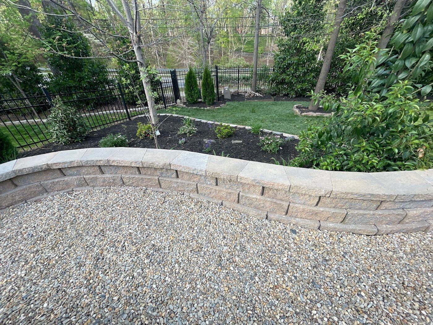 Gravel patio with a low retaining wall, leading to a landscaped garden area with trees and shrubs.