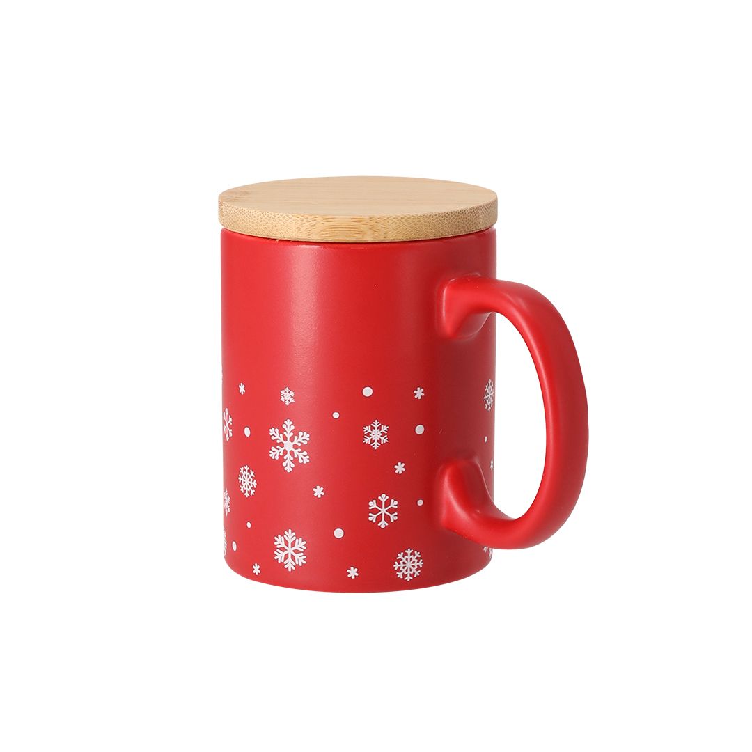 Una taza de cerámica roja con un estampado de copos de nieve blancos y una tapa de madera de color claro.